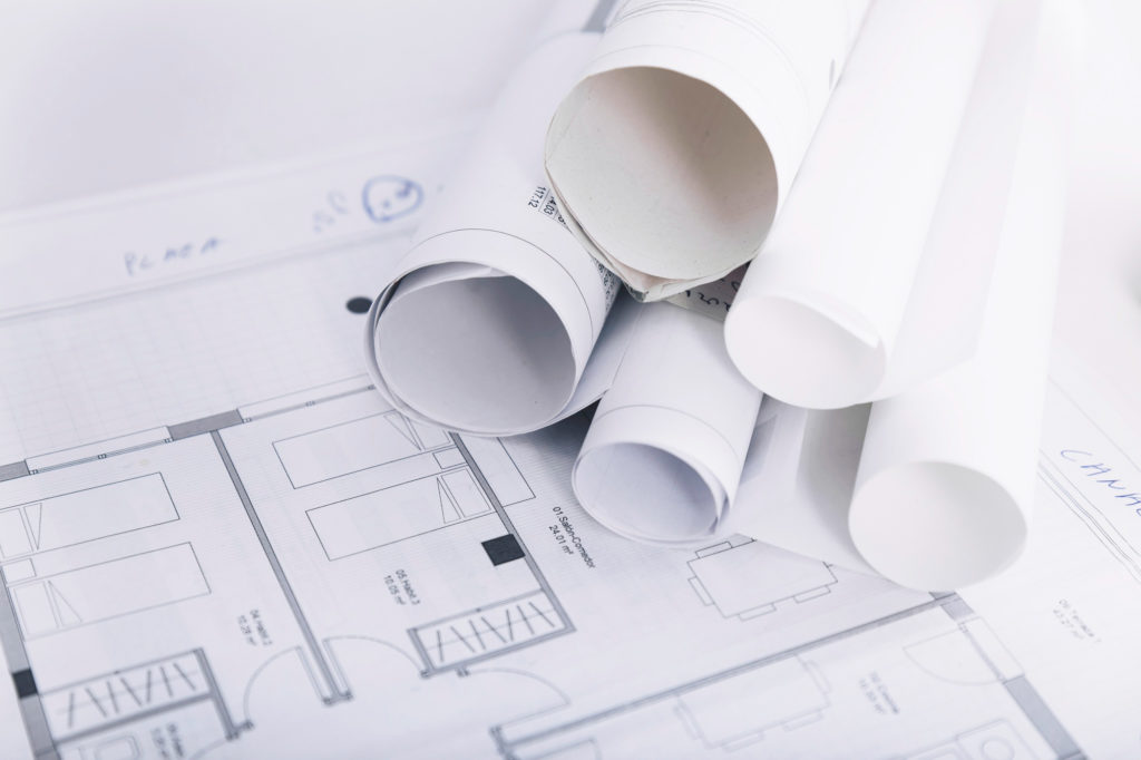 Plan d'architecte déplié avec 5 plans enroulés. Estimation immobilière en ligne vs estimation en présentiel. Poli Real Estate | Agence immobilière à Lausanne et Pully